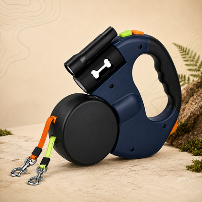 A retractable dog leash with a navy blue and black handle, a black reel, and bright orange and neon green straps, styled on a sandy surface with rocks and plants.