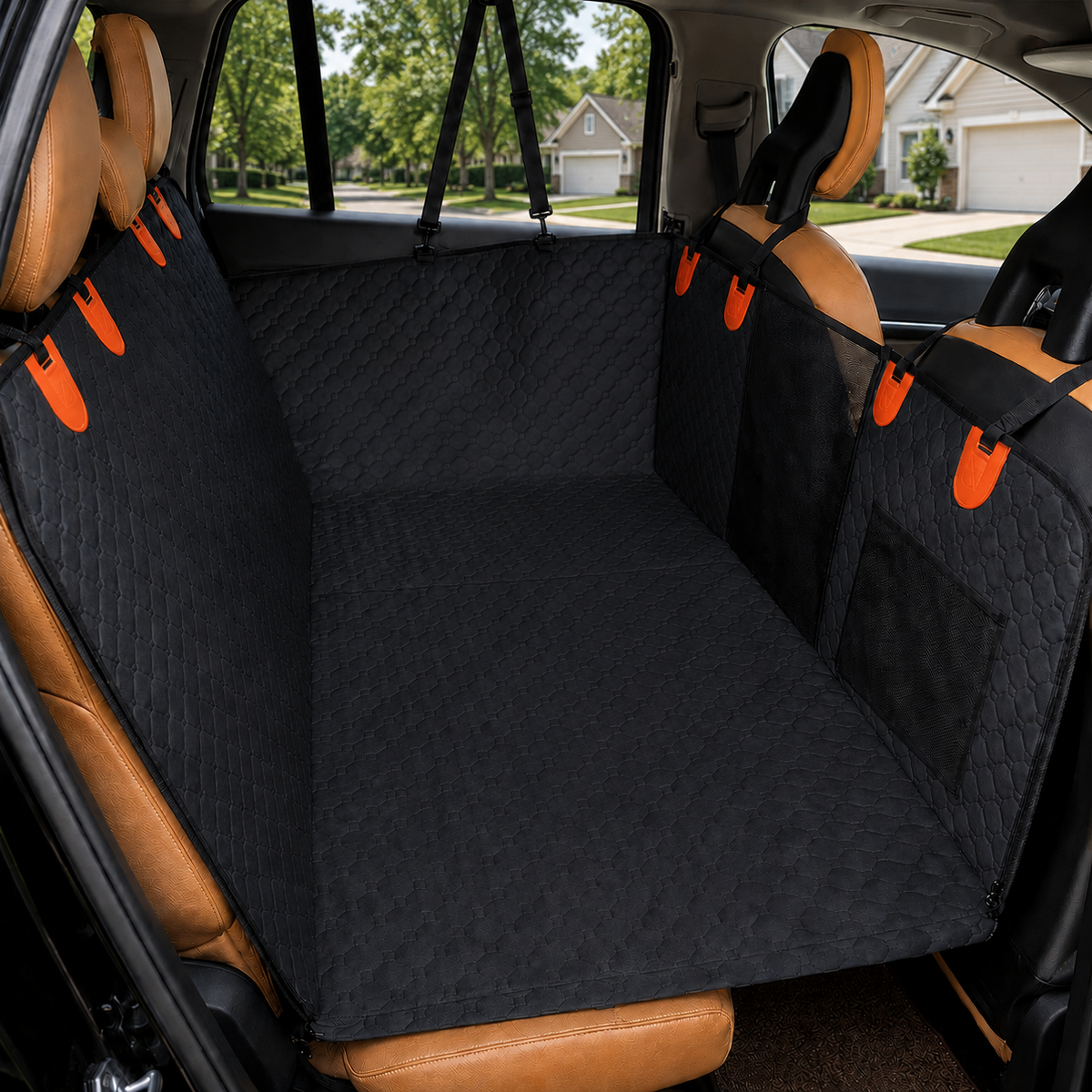 A black quilted car cargo liner set installed across the rear seats of a tan vehicle, with orange accent clips and side mesh pockets, shown in a real car interior with a suburban street visible through the windows.