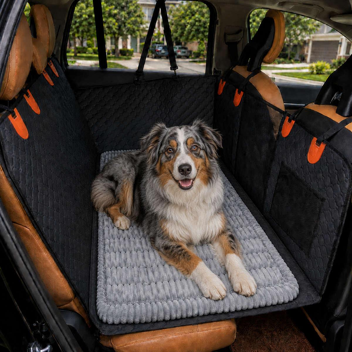 A dog lies on a gray ribbed pet mat inside a car's back seat area, surrounded by black quilted car seat covers with orange accents. The photo is taken in a real vehicle environment with trees and houses visible through the windows, so this is Lifestyle rather than Product/Packaging.